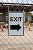 EXIT sign with an arrow pointing right on a chain-link fence at a construction site.