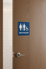 Wooden door with a restroom sign featuring gender-neutral symbols and the word 'RESTROOM'.