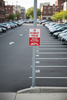 No overnight parking sign in a city parking lot with cars and buildings in the background.