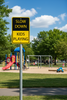 Yellow 'Slow Down Kids Playing' sign at a playground