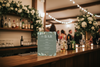 Bar setup with a decorative sign and floral arrangements.