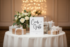 Table with 'Cards + Gifts' sign, flowers, and gift boxes against a blurred bokeh background