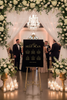 Decorative wedding setup with floral arch, chandelier, and seat plan board.