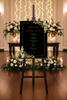 Wedding timeline board on an easel with floral decorations against a decorated background.